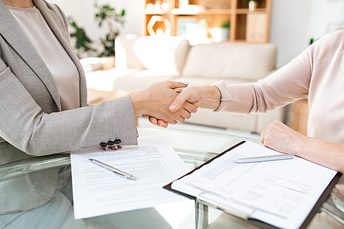 Handshake over table of young and mature females after negotiating and signing financial papers