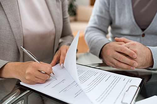 One of business partners putting signature on last page of financial contract after negotiation