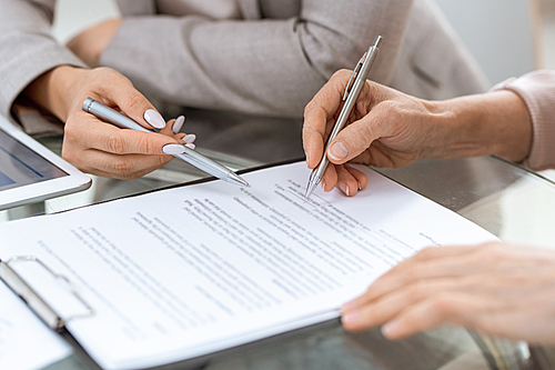 Human hands with pens over financial document in moment of putting signature after discussing its points