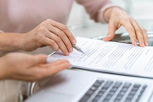 Hand of mature woman pointing at one of contract points while looking through the document before signing