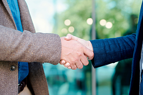 Handshake of two young successful business partners or colleagues after making deal or negotiating