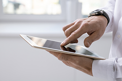 Hand of contemporary businessman with tablet pointing at screen during presentation or scrolling through online data