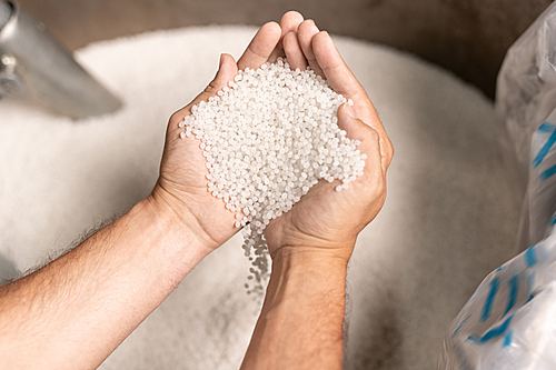 View of modern factory worker hands holding pile of white polymer pellets during working process
