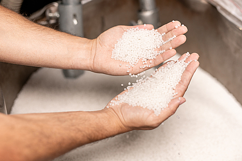 Human hands holding two piles of white polymer granules during quality control process at large factory