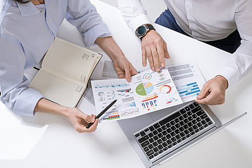 Hands of two contemporary brokers discussing financial documents with graphs, charts and diagrams at meeting