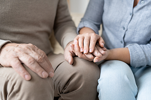 Hand of senior man in casualwear between those of his affectionate young daughter while both sitting close to each other