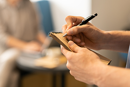 Waiter of modern cafe or restaurant holding pen over notepad page while going to make notes about order of client