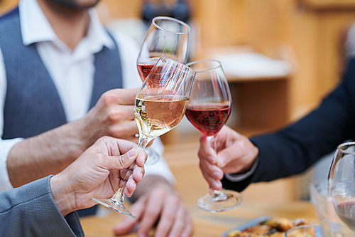 Three humans clinking with wineglasses of varoius sorts of wine while making celebratory toast