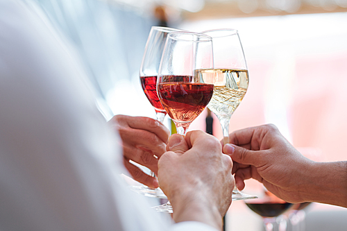 Human hands holding wineglasses with champagne, cabernet and brandy while clinking during toast
