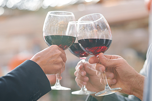 Hands of friends or business partners clinking with wineglasses with red wine while celebrating successful deal or other event