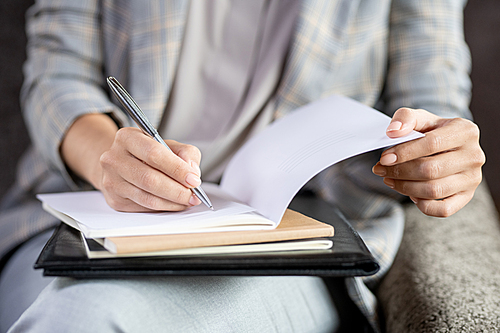 Contemporary young teacher holding pen over page of open copybook while checking paper of one of students