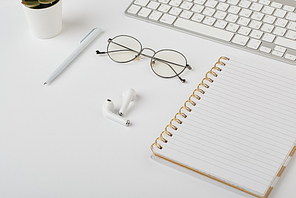 Wireless earphones, eyeglasses, pen, notebook and computer keypad on white desk that is workplace of office manager