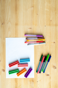 Overview of wooden table background with blank paper and several sets of colorful pencils and crayons