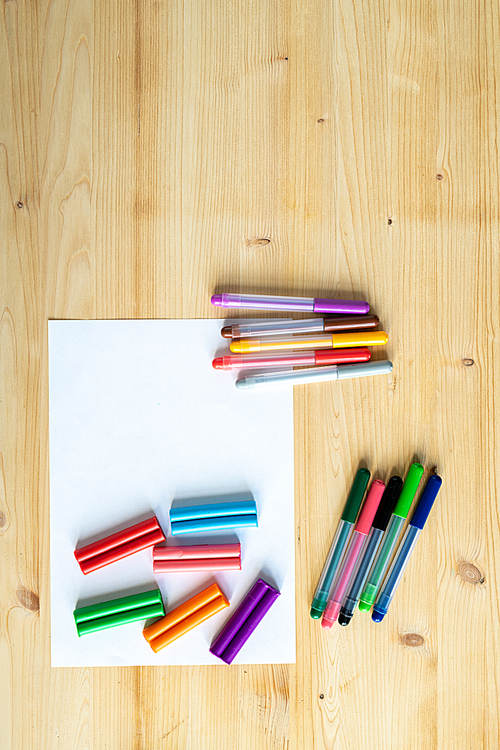 Overview of wooden table background with blank paper and several sets of colorful pencils and crayons