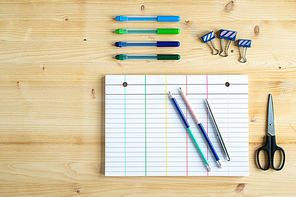 Stationary office supplies on wooden table - clips, scissors, blank notebook paper, pencils, pen and highlighters