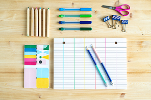 Top view of sheet of paper with lines surrounded by group of pencils and crayons with clips, scissors and set of erasers