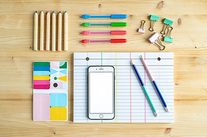 View of office or educational supplies on wooden table - several sets of crayons, smartphone, clips and lined paper