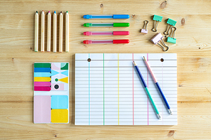 Blank lined page of notebook with two pencils and group of clips, sets of crayons and erasers near by