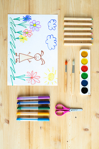 Overview of pencil drawing surrounded by watercolor paints, paintbrushes, scissors, crayons and highlighters