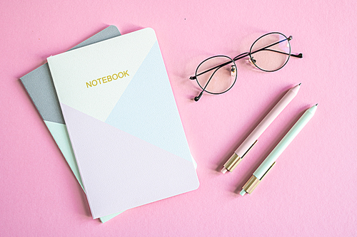 Top view of business person eyeglasses, two notebooks and pens over pink background