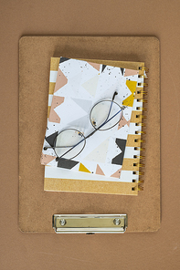 Overview of clipboard, notebook, notepad and eyeglasses on brown background or table