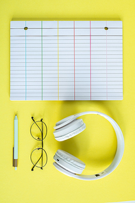 White headphones, eyeglasses, pen and lined page of notebook over yellow background