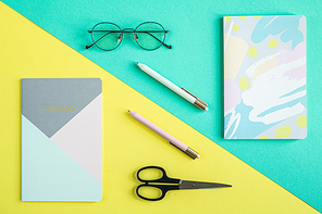 Two copybooks, pens, scissors and eyeglasses over blue and yellow backgrounds