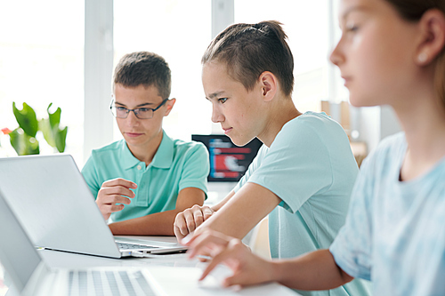 Group of contemporary learners of middle school looking at laptop display while working over project together