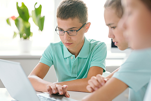 Two schoolboys concentrating on their schoolwork while sitting in front of laptop and looking through online information