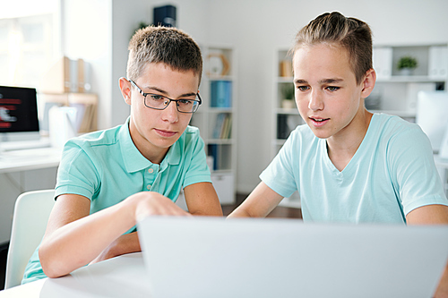 Two schoolboys discussing online data on laptop display while preparing school project or homework