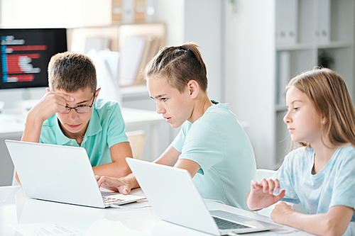 Cute schoolchildren sitting by desk in classroom while working over individual projects after classes