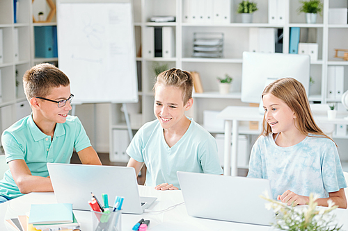 Group of contemporary schoolkids watching online video on laptop while preparing for school seminar