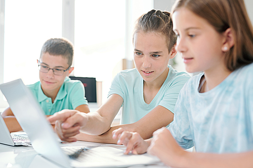 Clever boy pointing at laptop display while showing something to girl sitting next to him during discussion