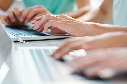 Hands of young students or schoolkids touching keys of laptop keypad while working in the net by desk at lesson