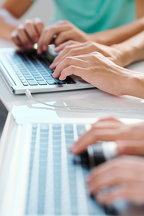 One of young contemporary co-workers or classmates typing on laptop keypad by desk at lesson