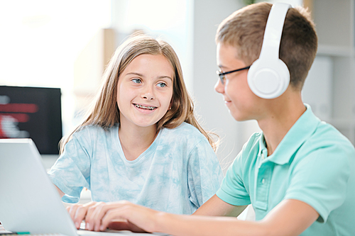 Two friendly classmates of middle school sitting in classroom while discussing data for seminar or next lesson