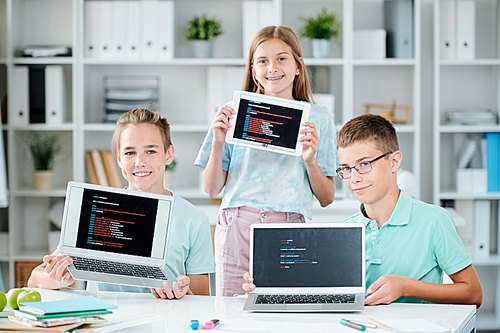 Three happy successful classmates showing their presentations on displays of mobile gadgets after finishing them up