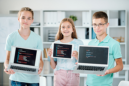 Group of youthful boys and girl holding laptops and touchpad while showing their final works at the end of school year