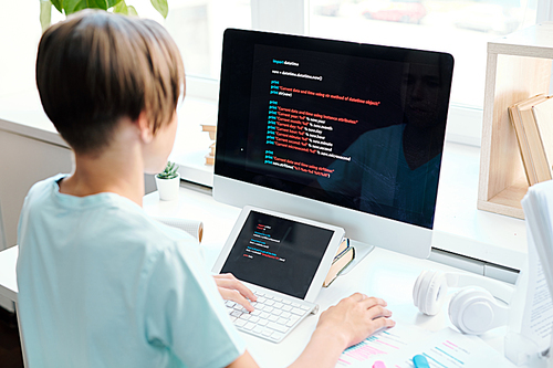 Contemporary schoolboy sitting by desk in front of computer monitor while analyzing data or preparing report for seminar