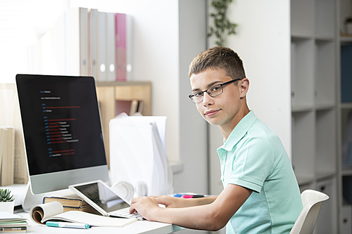 Serious youthful middle school student sitting by desk in front of computer monitor and working over project