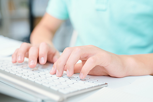 Human hands pushing keys of computer keyboard while sitting by desk in classroom or office