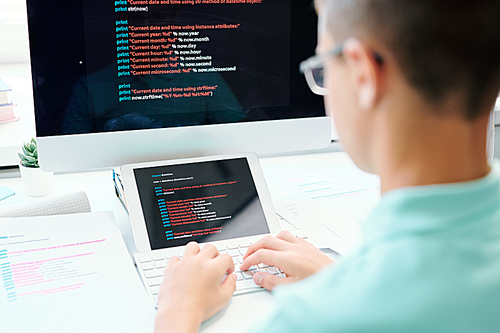 Young male sitting by workplace while pressing computer keypad buttons and entering data