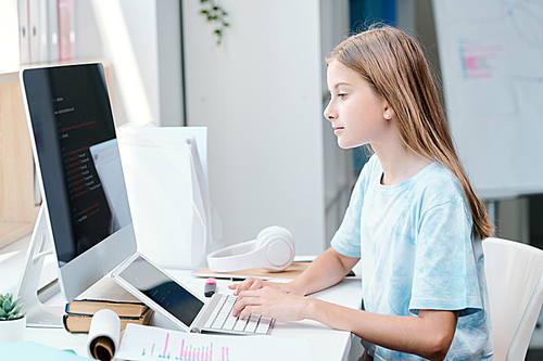 Serious clever schoolgirl looking at online data on computer screen while analyzing it or choosing for her report