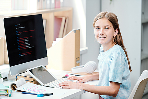 Happy schoolgirl  while sitting by desk and preparing for school seminar in computer classroom