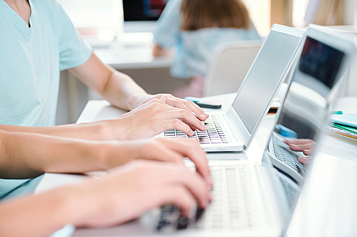 Two contemporary students of school or college typing on laptop keypads at lesson or preparing for seminar