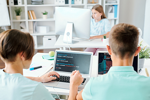 Two schoolboys sitting by desk in front of laptops with schoolgirl networking by computer monitor on background