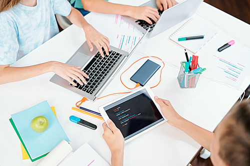 Hands of three clever school learners with modern mobile gadgets over desk during network or preparation of homework