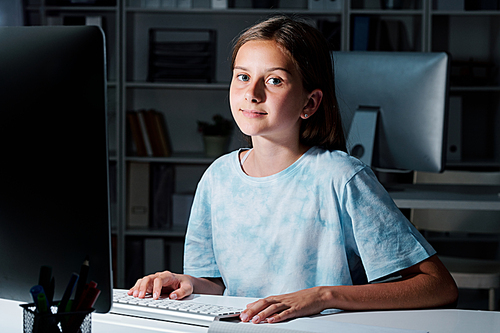 Cute middle school student looking at you while preparing for seminar late in the evening in classroom