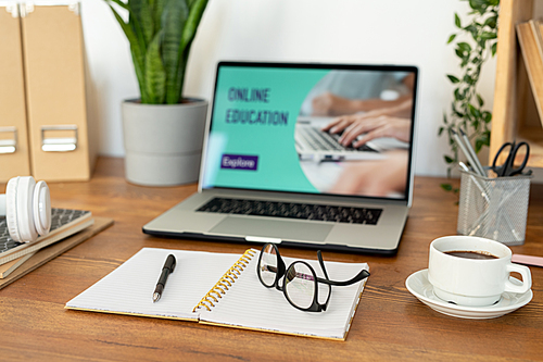 Open notebook with pen and eyeglasses on blank pages and cup of coffee on background of laptop