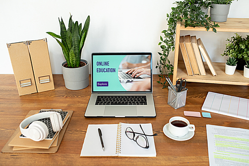 Group of office supplies and objects on the desk in front of laptop with website homepage on its display